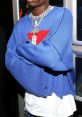 Playboi Carti in a stylish blue sweater, showcasing streetwear vibes and bold accessories at a lively event.