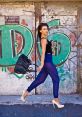 Fashionable model Codie Phillips struts in sheer blue pants and heels against vibrant graffiti backdrop, showcasing trendy urban style.