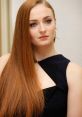 Sophie Turner with long red hair, wearing a stylish black dress, showcasing a natural yet elegant look.