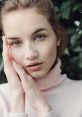 Portrait of a girl with soft features, wearing a cozy pink sweater, showcasing natural beauty against a green backdrop.