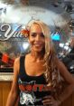 Mandy Gubler smiling in a Hooters shirt, with long hair and a flower accessory, in a West Virginia venue.