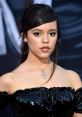 Jenna Ortega with a chic hairstyle and elegant black off-shoulder dress, showcasing her striking makeup and necklace.