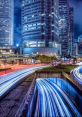 Vibrant cityscape at night, showcasing illuminated skyscrapers and light trails of traffic on bustling urban roads.