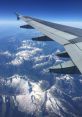 Airplane wing over stunning snow-capped mountains under a clear blue sky, showcasing aerial views from high altitude.