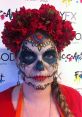 Vibrant Dia de los Muertos makeup featuring intricate sugar skull design and red floral headdress, capturing cultural celebration.