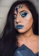 Glamorous water-themed makeup with blue tones, jeweled accents, and dramatic tear designs for a stunning creative look.