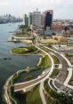 Aerial view of a waterfront area featuring park paths, greenery, and modern buildings along the river's edge.