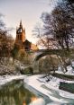 Historic bridge over the snow-covered River Kelvin with a majestic church spire in the background during winter.