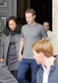 Mark Zuckerberg, casually dressed, exits a building alongside a woman, surrounded by others, in a candid moment.