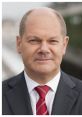 Olaf Scholz, German Chancellor, dressed in formal suit and patterned tie, poses confidently outdoors with a neutral background.