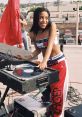 Aaliyah Haughton spinning records on turntables, showcasing her hip hop and R&B style in vibrant Tommy Hilfiger attire.