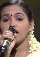 Singer performing on stage with microphone, adorned in traditional attire and floral jewelry, showcasing Indian vocal talent.