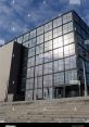 Modern architecture of a Croatian library featuring glass facade and steps against a cloudy blue sky.