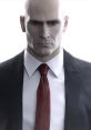 Agent 47, portrayed by David Bateson, exudes a cool, intimidating presence in a formal suit with a red tie.