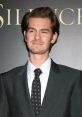 Andrew Garfield smiles confidently in a stylish suit at a film premiere, showcasing his charismatic on-screen presence.