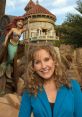 Jodi Benson smiles in front of Ariel's castle, celebrating her role as the voice of The Little Mermaid at a themed event.