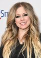 Avril Lavigne smiles confidently, showcasing her wavy hair and striking makeup at a recent event.