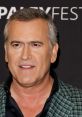 Bruce Campbell smiling at a red carpet event, showcasing his iconic style and charm, a beloved figure in horror cinema.