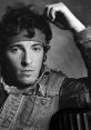 Black and white portrait of Bruce Springsteen, wearing a bandana and denim jacket, capturing his iconic rock star essence.