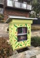 Colorful little free library on a residential street, filled with books and surrounded by lush greenery. Community reading space.