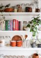 Organized kitchenware library with glass jars, terracotta bowls, cookbooks, and greenery for a stylish cooking space.