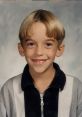 Smiling young boy with a bowl haircut, wearing a black and white zip-up jacket, exuding a cheerful vibe.