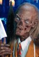 Crypt Keeper with a sinister grin, holding a knife, featuring eerie blue eyes and spooky costume in a haunted setting.