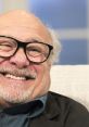 Danny DeVito smiling warmly, wearing glasses, showcasing his charming personality during a light-hearted interview.