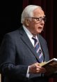 David McCullough speaking at an event, holding a book, showcasing his contribution to historical literature.