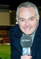 Derek Rae, FIFA commentator, smiles while holding a BT Sport microphone at a football event, showcasing his broadcasting passion.