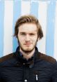 Felix "Pewdiepie" Kjellberg winks playfully, wearing a dark jacket against a blue and white striped background.