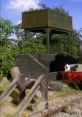 Henry from Thomas & The Magic Railroad near a water tower, surrounded by lush greenery and railway tracks.