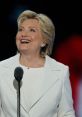 Hillary Clinton smiles while speaking at a podium, showcasing her passionate speech delivery and charismatic presence.