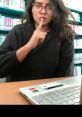 Person making a shushing gesture in a library setting, emphasizing quietness while using a laptop. Boob Tube Library.