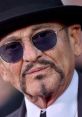 Joe Pesci poses confidently in a stylish black hat and sunglasses, showcasing his iconic look.