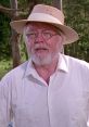 John Hammond, the visionary founder of Jurassic Park, in a straw hat and white shirt, surrounded by lush greenery.