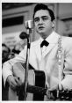 Johnny Cash performs passionately in a white suit, holding a guitar, with a vintage microphone in a lively setting.