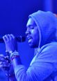 Kanye West performing passionately in a blue-lit setting, wearing a hoodie and holding a microphone.