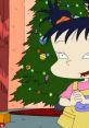 Kimi Finster, cheerful and animated, stands by a decorated Christmas tree with colorful ornaments and lights.