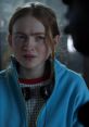 Max from Stranger Things looks distressed, wearing a blue jacket and headphones, deep in conversation with someone.