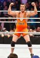 Michael Cole, WWE commentator, flexes muscles in orange wrestling attire, energizing the crowd in a wrestling ring.