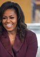 Michelle Obama smiles warmly, wearing a stylish top and a "Becoming" necklace, exuding charisma and confidence.