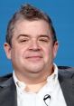 Patton Oswalt smiles in a casual setting, showcasing his distinctive hairstyle and warm personality.