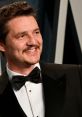 Pedro Pascal smiling in a formal black tuxedo, showcasing his charming personality at a glamorous event.