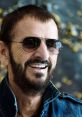 Ringo Starr smiles while wearing sunglasses and a denim jacket, showcasing his signature style and iconic persona.