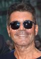 Simon Cowell smiling with sunglasses at a public event, showcasing his iconic style and confident personality.