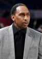 Stephen A. Smith in a stylish plaid suit, engaged in intense sports commentary at a basketball event.