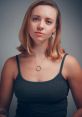 Portrait of a young woman with shoulder-length hair, wearing a gray tank top and pendant necklace, exuding confidence and elegance.