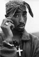 Tupac Shakur wearing a bandana and cross necklace, showcasing his iconic style and charisma in black and white portrait.