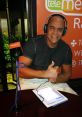 Waldemaro Martinez, radio host, gives a thumbs up while wearing headphones in a vibrant studio setting.